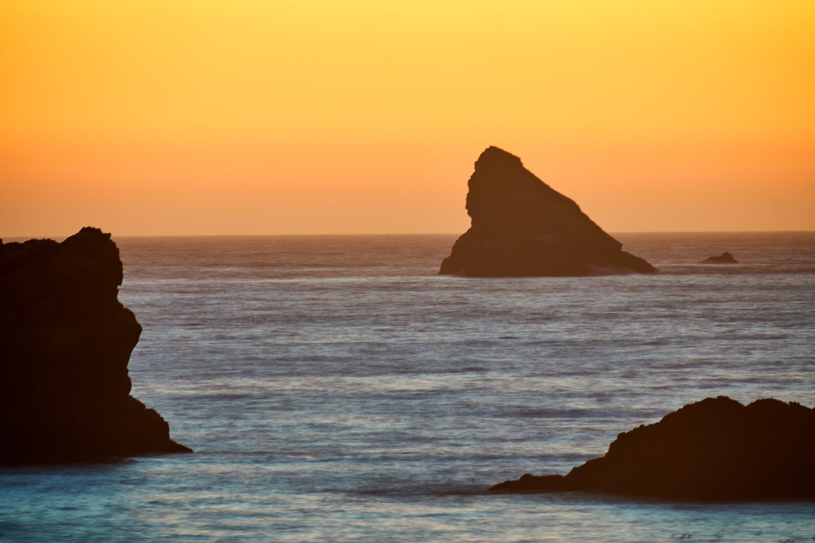 A sea stack against an orange sunset
